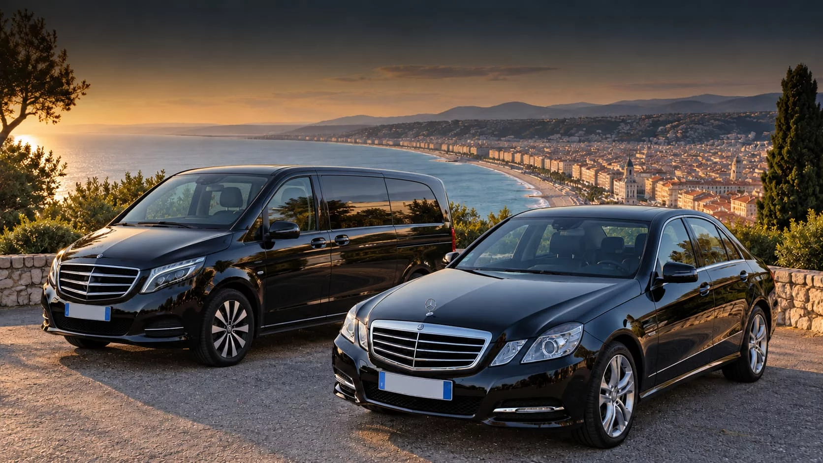 Van et berline Mercedes noirs devant un panorama de bord de mer au coucher du soleil.